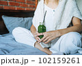 Crop photo of Young woman in casual clothes with green smoothie sitting on bed at the home 102159261