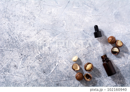 Natural macadamia nut oil in a bottle. Cosmetic oil. Top view macadamia nuts on a gray background. 102160940