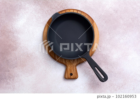 Cast iron skillet on a wooden cutting board on light background. Kitchen utensils. Empty place. Top view. 102160953