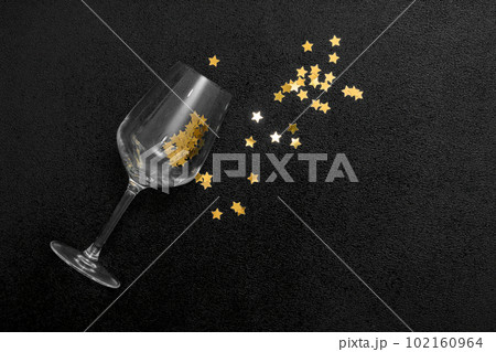 Glass empty goblet. Confetti stars inside the glass. Golden decor on a black background. Glass empty goblet. Confetti stars inside the glass. Golden decor on a black background. 102160964