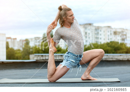 A man practices yoga on the roof of the house. Yoga at sunset. Healthy life, sport and meditation concept. 102160985