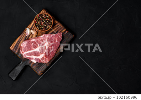 Raw pork steak on a wooden cutting board. Meat, dry pepper mixture, garlic on a black background. View from above. 102160996