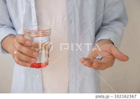 The man's hands are holding a glass of water and pills. The man's hands are holding a glass of water and pills. 102162367