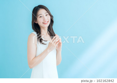 日差しが差し込むブルーバックでスキンケアをする若い女性 102162842