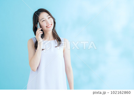 日差しが差し込むブルーバックでスマホを操作する若い女性 102162860