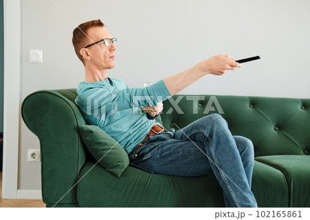 Man pointing tv remote control sitting on sofa in living room 102165861