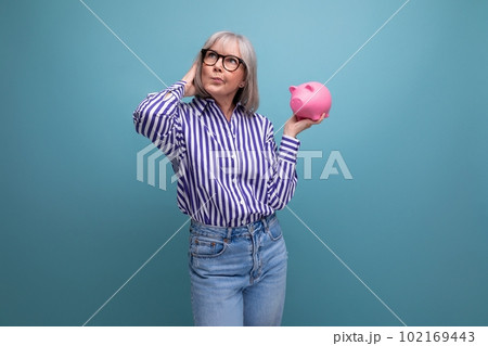 smart 60s woman with gray hair holding piggy bank on bright studio background 102169443