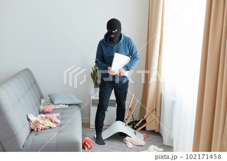 Dengerous man in a black mask and blue hoodie enters someone else's house to rob the owners, breaking apartment for stealing someone else property, holding laptop and going away. Dengerous man in a black mask and blue hoodie enters someone else's house to rob the owners, breaking apartment for stealing someone else property, holding laptop and going away. 102171458