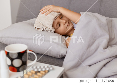 Side view of sick unhealthy little baby girl with fever, having wet towel on her forehead to lower the temperature, child taking medicine, suffering from influenza. Side view of sick unhealthy little baby girl with fever, having wet towel on her forehead to lower the temperature, child taking medicine, suffering from influenza. 102171656