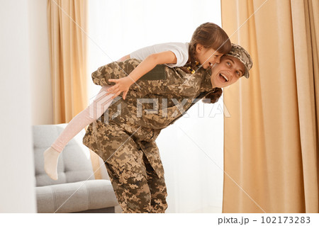 Excited mother and her charming daughter playing together indoor near window, little cute girl pretending to be like a plane while sitting on mommy's back. 102173283