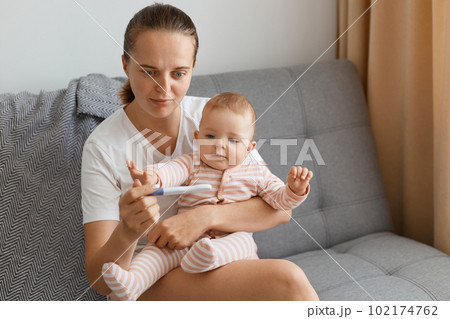 Astinished Caucasian beautiful woman wearing wnhite t shirt got shocked when pregnancy test showing positive result, young mother holding toddler baby girl in hands while sitting on sofa at home. Astinished Caucasian beautiful woman wearing wnhite t shirt got shocked when pregnancy test showing positive result, young mother holding toddler baby girl in hands while sitting on sofa at home. 102174762