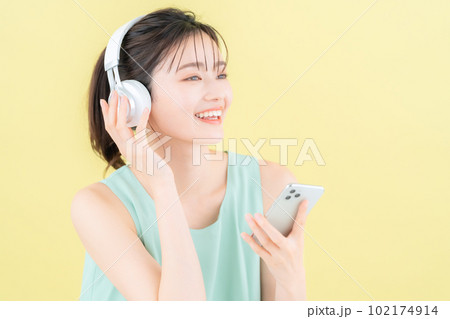 イエローバックでヘッドフォンをつけて音楽を聴く若い女性 イエローバックでヘッドフォンをつけて音楽を聴く若い女性 102174914