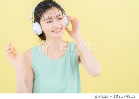 イエローバックでヘッドフォンをつけて音楽を聴く若い女性 イエローバックでヘッドフォンをつけて音楽を聴く若い女性 102174915