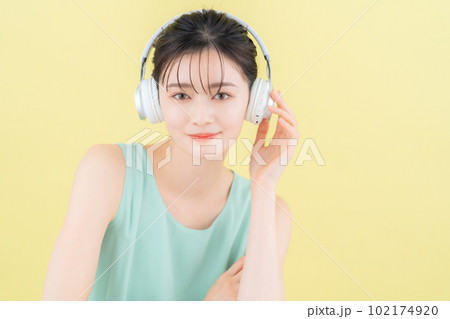 イエローバックでヘッドフォンをつけて音楽を聴く若い女性 102174920