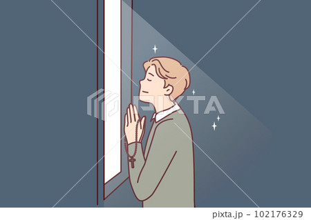 Religious man prays standing at window and holds chain with catholic christian crucifix in hands Religious man prays standing at window and holds chain with catholic christian crucifix in hands 102176329