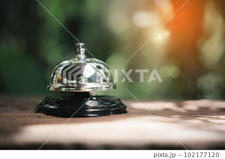 Hotel ring bell. Vintage bell to call staff outdoor in garden with green leaf, Closeup of silver service restaurant bell on wooden counter desk 102177120