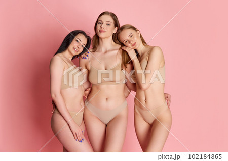 Portrait with group of young girls wearing beige underwear posing over pink studio background. Female body 102184865