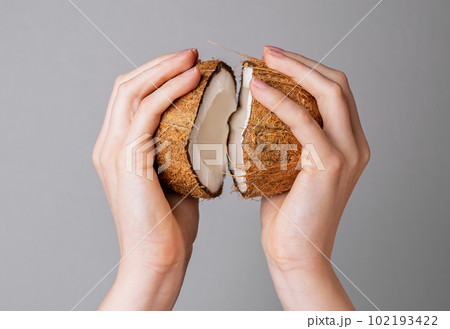 Hands opening coconut, two pieces halves of coco nut fruit in brown shell Hands opening coconut, two pieces halves of coco nut fruit in brown shell 102193422