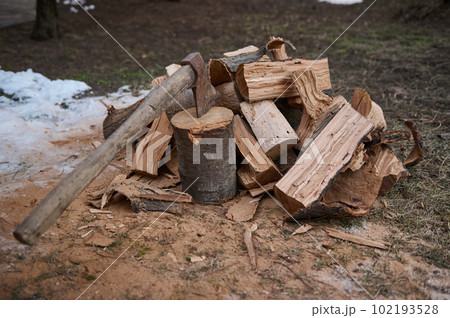 Still life with a wood-burning wooden handle axe for making fire and firewood for fire heat in the winter in a rustic style. Ax and firewood in the yard. Cutting wood in the forest for making fire Still life with a wood-burning wooden handle axe for making fire and firewood for fire heat in the winter in a rustic style. Ax and firewood in the yard. Cutting wood in the forest for making fire 102193528