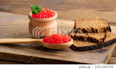 Red caviar in a wooden spoon, slices of bread on the table 102198149