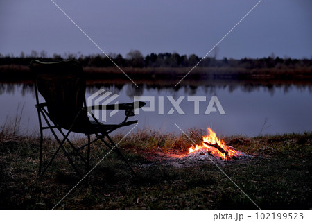 Tourist chair, folding chair, bonfire on the river bank in late evening, twilight in the fall at sunset, relaxation and rest, early autumn, close-up Tourist chair, folding chair, bonfire on the river bank in late evening, twilight in the fall at sunset, relaxation and rest, early autumn, close-up 102199523