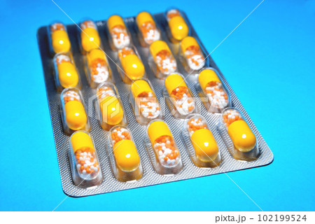 capsules in a blister, a medicine, tablets, vitamins in the form of granules in a yellow capsule, blur as a creative technique of the author, close-up 102199524