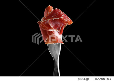 Tasty prosciutto on fork against black background 102200103