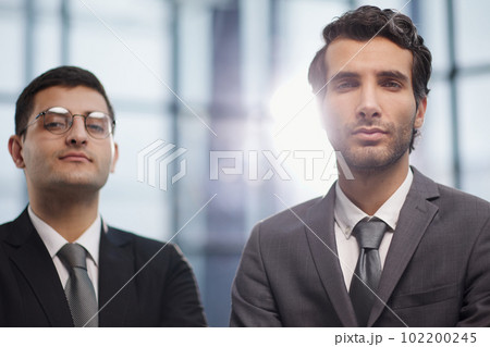 Two serious young businessmen standing with arms crossed in office Two serious young businessmen standing with arms crossed in office 102200245