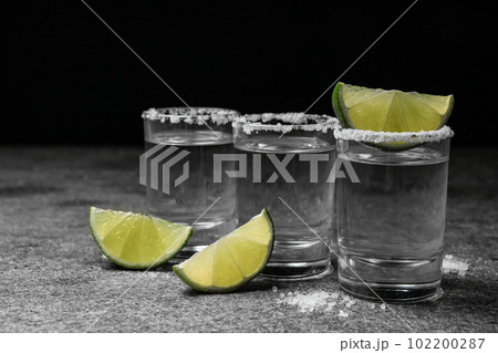 Mexican Tequila shots with salt and lime slices on grey table 102200287