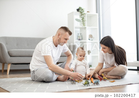Mother and father with baby putting toys on carpet at home Mother and father with baby putting toys on carpet at home 102200417