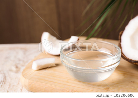 Coconut oil in glass bowl on wooden board, closeup 102200600