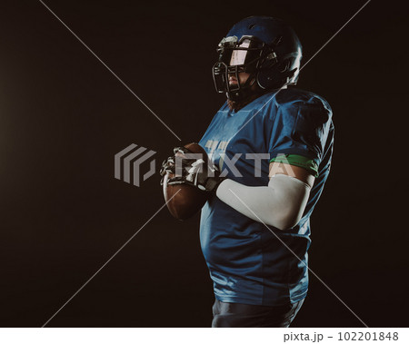 An Asian man with a red beard in a blue American football uniform throws a ball against a black background. An Asian man with a red beard in a blue American football uniform throws a ball against a black background. 102201848