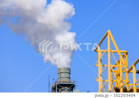 白い煙を吹き上げる工場の煙突と黄色い手すり 102203404