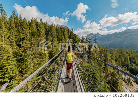 Woman hiking in mountains crossing foot suspension bridge with amazing views. Canada Tourism concept from British Columbia. Hiker tourist in breathtaking nature in outdoor paradise Squamish, BC 102209135