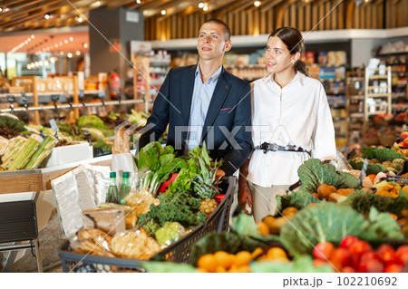 Adult couple is standing with cart with products in supermarket 102210692