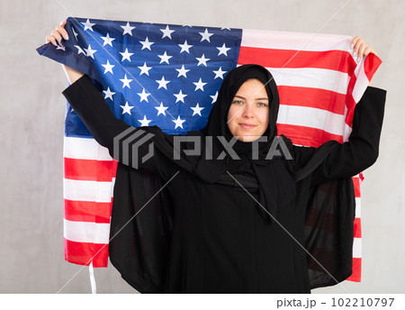 Happy young woman dressed in traditional islamic clothes with american flag 102210797