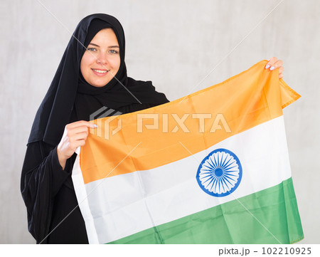 Balanced smiling Muslim woman in traditional black hijab holds flag of India Balanced smiling Muslim woman in traditional black hijab holds flag of India 102210925