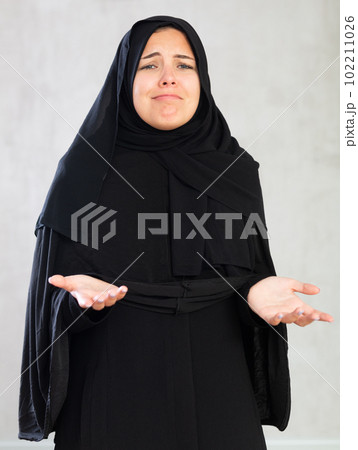 young Muslim woman in black hijab is upset by bad news and dejectedly holds her hands palms up. young Muslim woman in black hijab is upset by bad news and dejectedly holds her hands palms up. 102211026