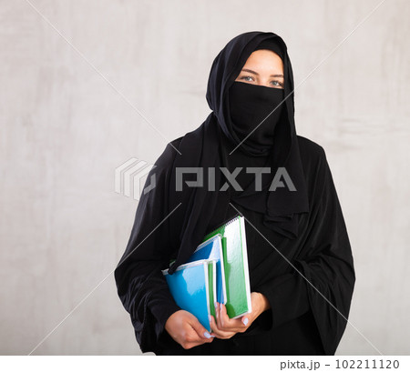 girl with face covered with burka holds lot of thick notebooks. foreign girl with face covered with burka holds lot of thick notebooks. foreign 102211120