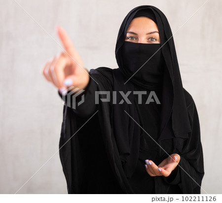 woman with her face covered by burka points her hand to side woman with her face covered by burka points her hand to side 102211126