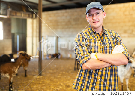 Portrait of positive male farmer standing with crossed hands on chest and smiling at camera on on cattle farm 102211457