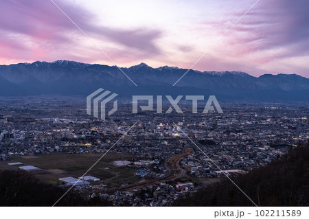 《長野県》北アルプスの山並みと松本市の街並み・夕暮れ 102211589