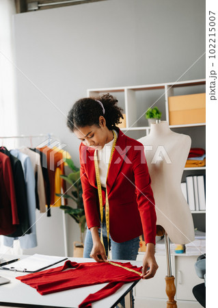 Calm curly brunette dark skinned woman on desk in office of fashion designer and holds tablet and smartphone. 102215007