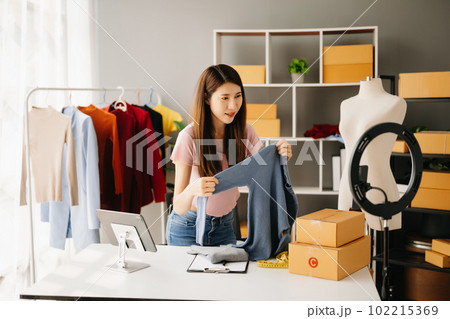 Fashion blogger concept, Young Asian women selling clothes on video streaming.Startup small business SME, using smartphone or tablet taking receive and checking. 102215369