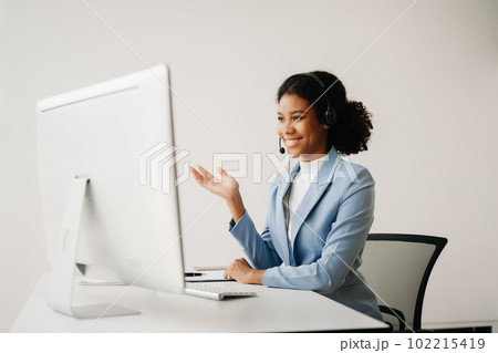 Serious call center operator in wireless headset talking with customer, woman in headphones with microphone consulting client on phone in customer support service in business center 102215419