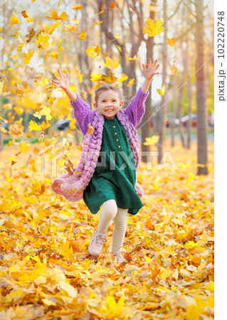 Joyful laughing caucasian girl 5 y.o. having fun in autumn park throws up fallen leaves 102220748
