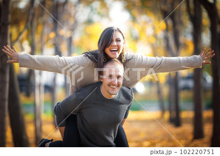 Happy caucasian man carrying his asian girlfriend on back in autumn outdoor 102220751