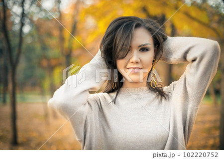 Young beautiful mixed race woman 30s in gray sweater posing in autumn park looking at camera 102220752