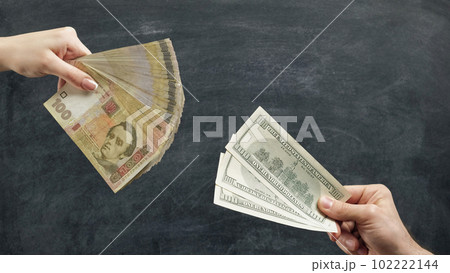 Money trade. Currency exchange. Woman hand giving hryvnia banknotes for man with dollars on chalkboard background. Money trade. Currency exchange. Woman hand giving hryvnia banknotes for man with dollars on chalkboard background. 102222144