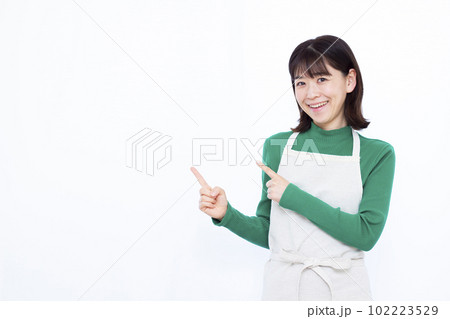 白い背景の前で指を指しているエプロン姿の30代の主婦 白い背景の前で指を指しているエプロン姿の30代の主婦 102223529